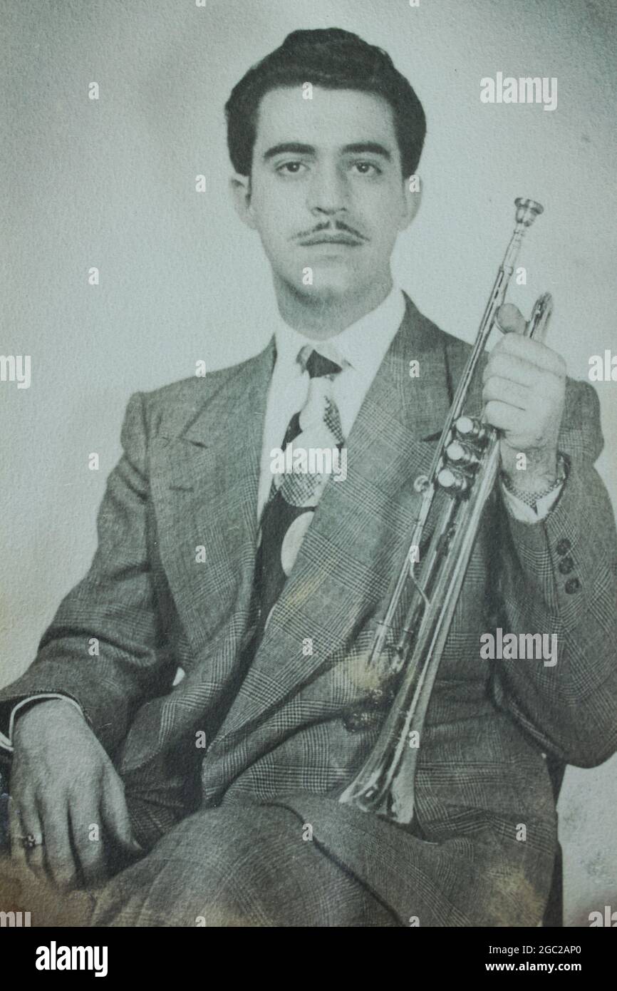 An old photo of a young man posing for a formal portrait while holding his trumpet in his hand. Stock Photo
