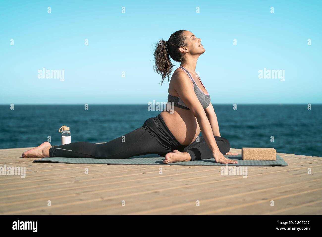 Young pregnant woman doing prenatal pilates exercises session next the sea - Health lifestyle and maternity concept Stock Photo