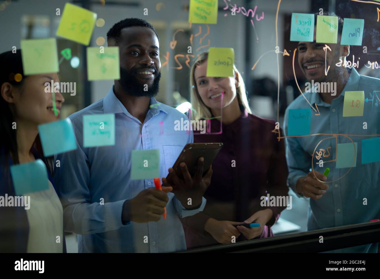 Diverse male and female business colleagues reading colourful memo notes on glass wall Stock Photo