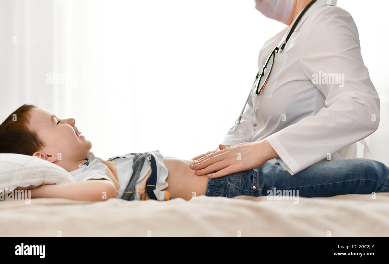 The doctor palpates the baby's stomach, which is filled with laughter in the rays of light from the window. Stock Photo