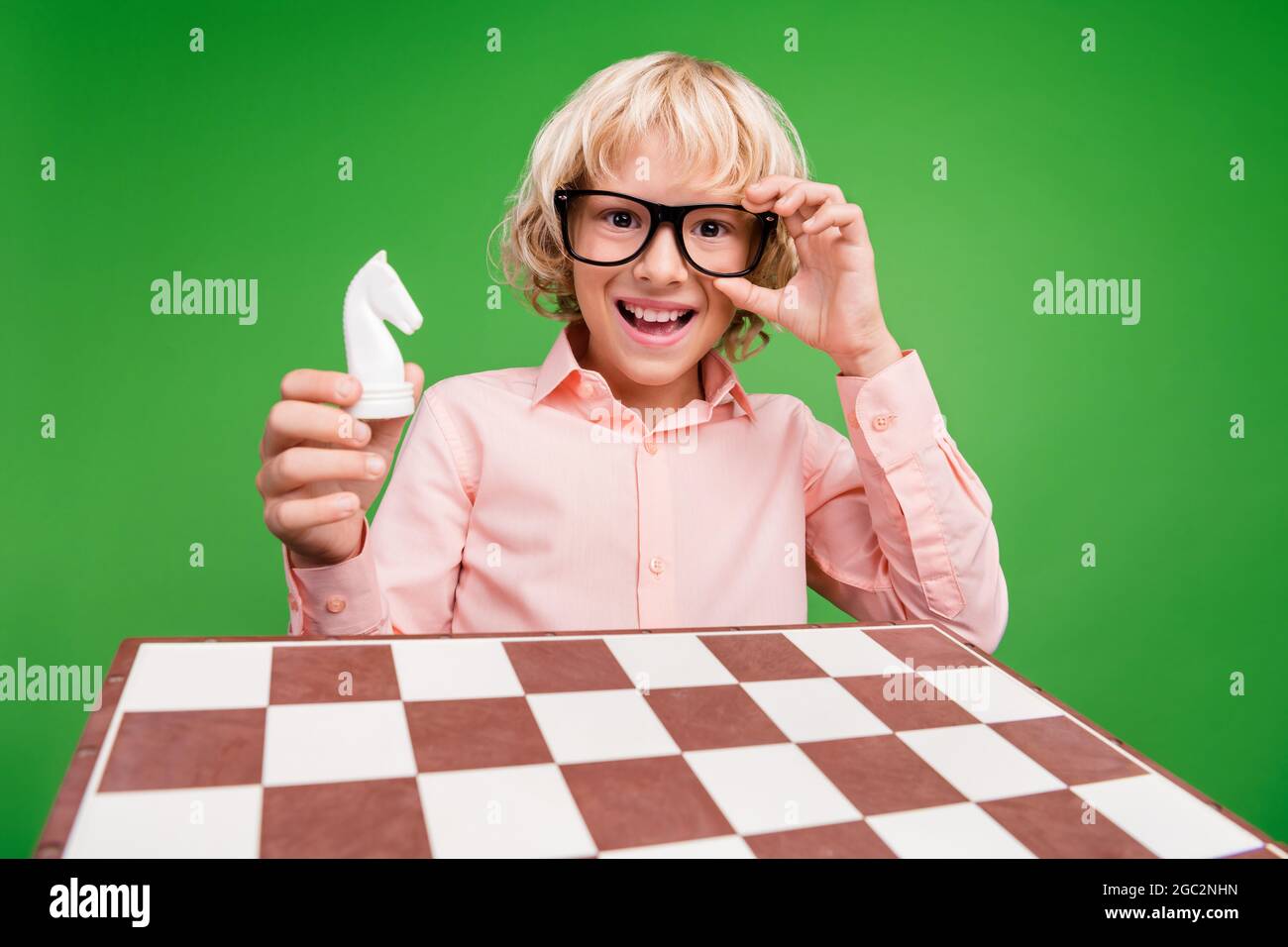 Photo of positive cheerful happy boy hold hand horse figure chess smile isolated on green color background Stock Photo