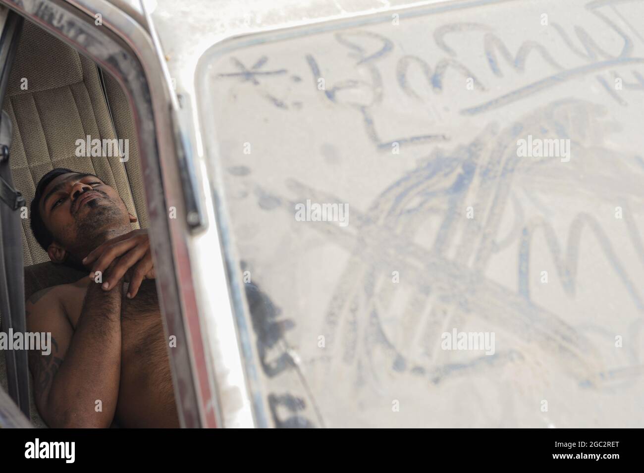 16.02.2014, Yangon, Myanmar, Asia - A man snoozes in the front seat of a parked automobile with its dirty windscreen completely covered in street dust. Stock Photo