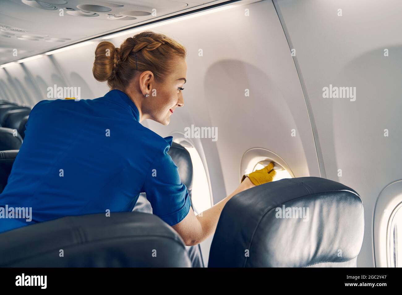 Smiling air hostess closing the window shade Stock Photo