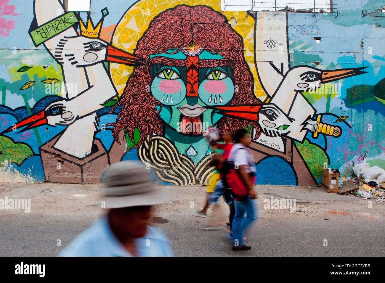 Locals pass by a colourful street art mural in Cartagena, Colombia. Stock Photo