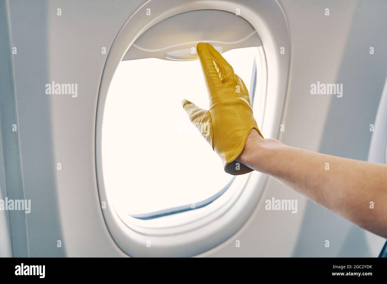 Gloved hand closing the window shades on the airplane Stock Photo