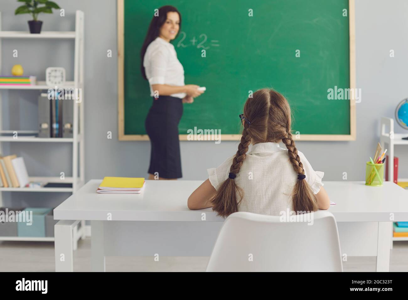 Schoolkid sitting at desk and listening attentively to teacher in modern classroom Stock Photo