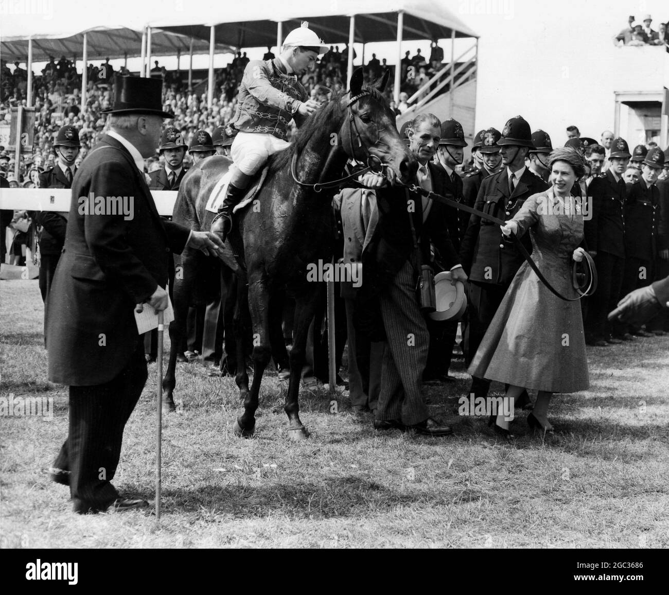 HM Queen Elizabeth II leads her horse Carrozza in after it has won the 179th Oaks Stakes, with Lester Piggott in the saddle. On the left is Lord Rosebery, a course steward, and in the centre is the Queen's trainer Mr Noel Murless. In a photo-finish, Silken Gilder, ridden by J Eddery, was given second, and Rose Royal II, the favourite with J Massard in the saddle, third. 7th June 1957 Stock Photo