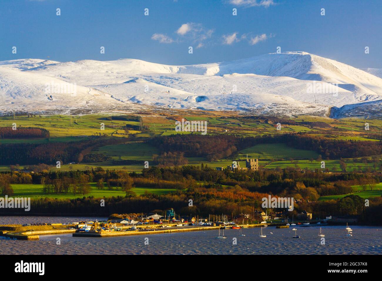 Bangor Port and Penrhyn Castle from across Menai Strait with snow on mountains of Snowdonia beyond in winter seen from Menai Bridge Gwynedd Wales UK Stock Photo