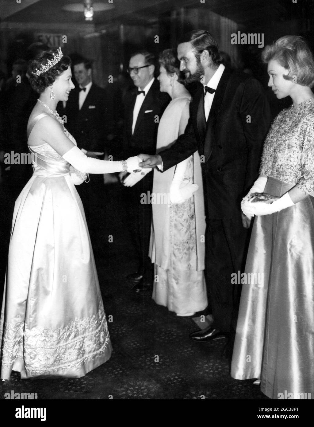 Her Majesty The Queen Elizabeth II at film premiere shakes hands with Stanley Baker one of the stars in the the film The Guns of Navarone on the right is Mrs Stanley Baker 27 April 1961 Stock Photo