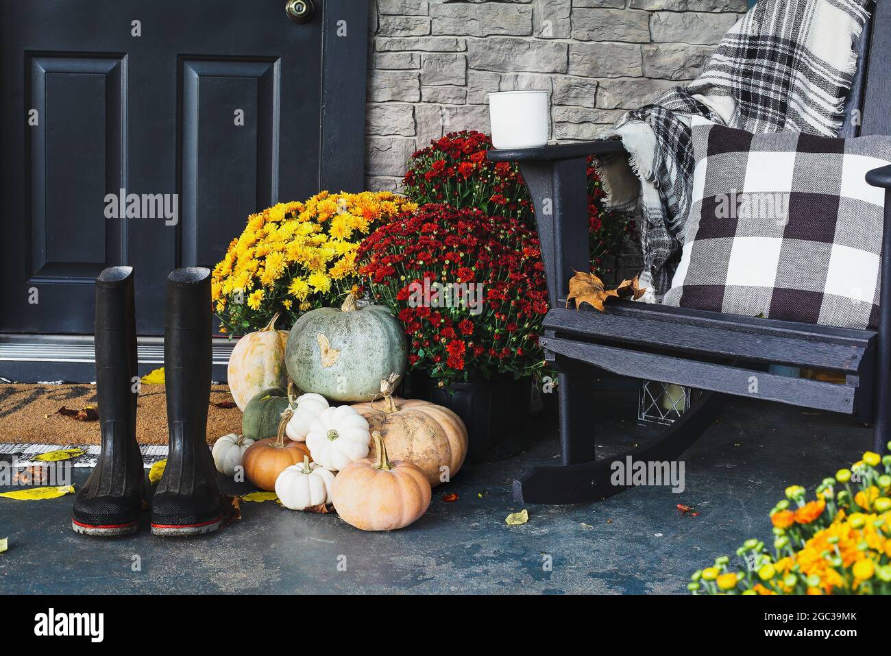 Hot steaming coffee sitting on rocking chair on front porch that has been decorated for autumn with heirloom white, orange, grey pumpkins, rain boots Stock Photo