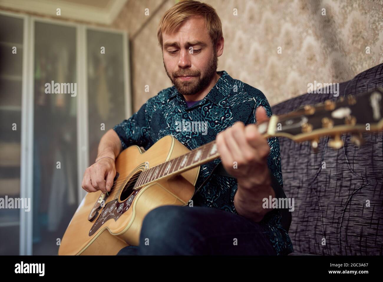 Adult male musician playing acoustic guitar and singing song into microphone while rehearsing in retro apartment Stock Photo