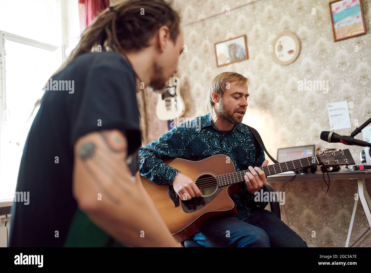 Man with dreadlocks beating rhythm while male friend playing guitar during rehearsal in vintage apartment Stock Photo