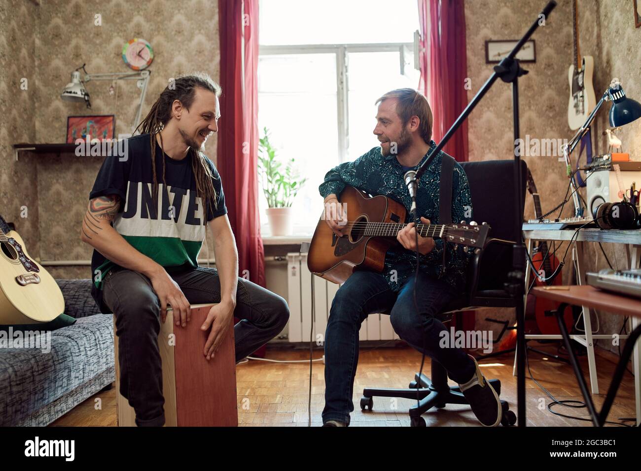 Man with dreadlocks beating rhythm while male friend playing guitar during rehearsal in vintage apartment Stock Photo
