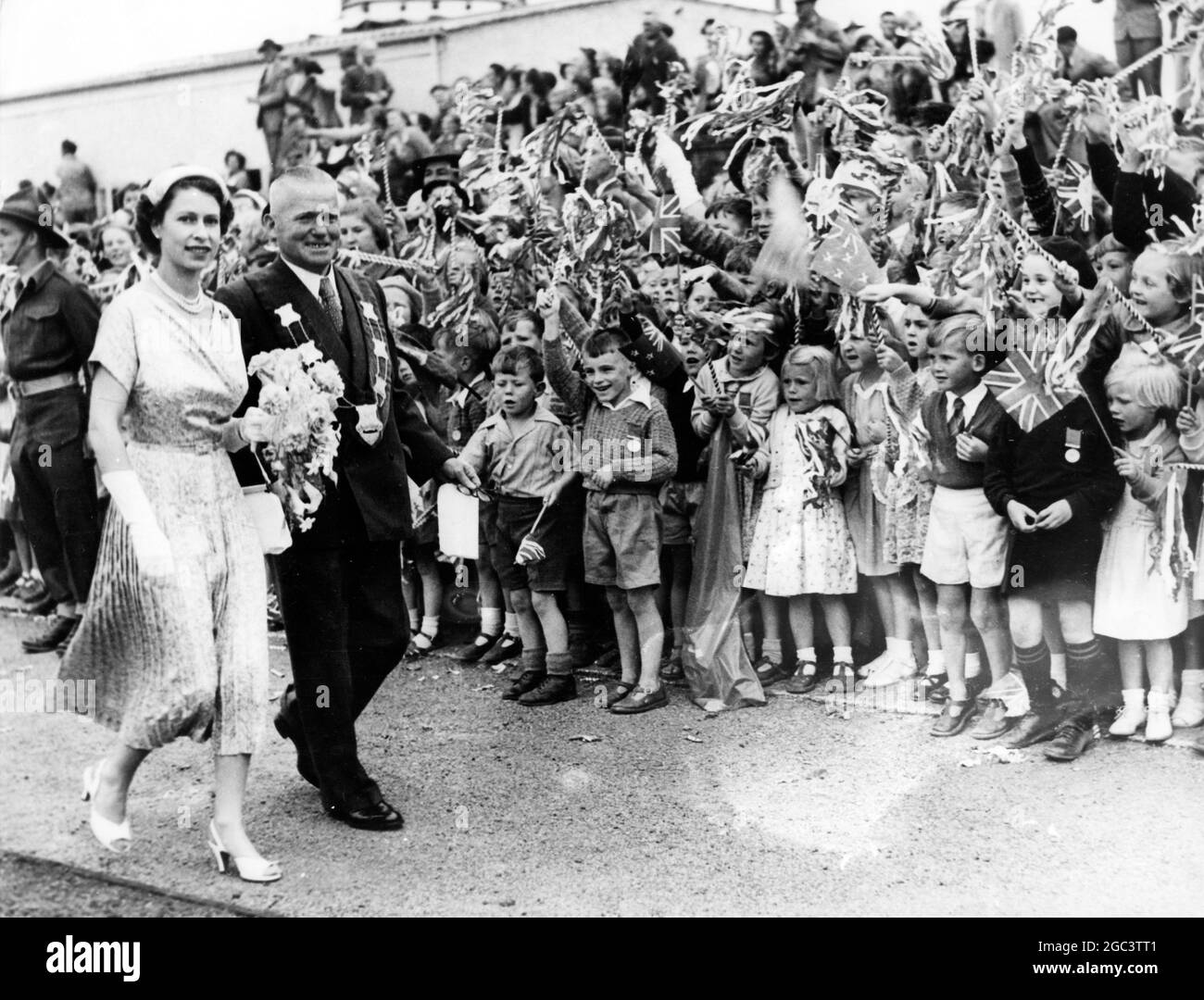 Queen Elizabeth II , escorted by the Mayor of Waipukurau , passes through lanes of cheering children on their tour of New Zealand . 12 Janaury 1954 Stock Photo