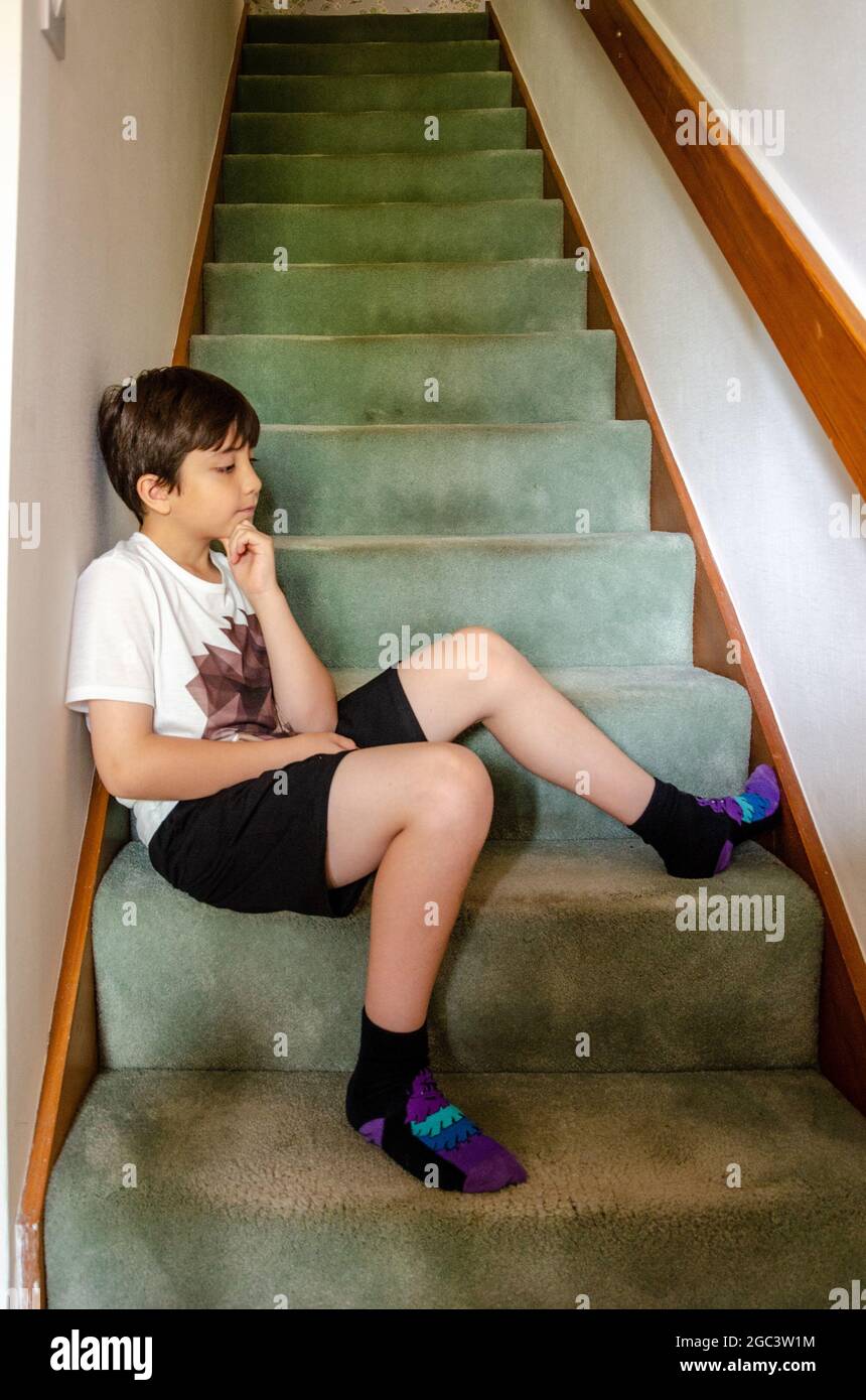 A young boy sits on the bottom steps of a flight of stairs at home