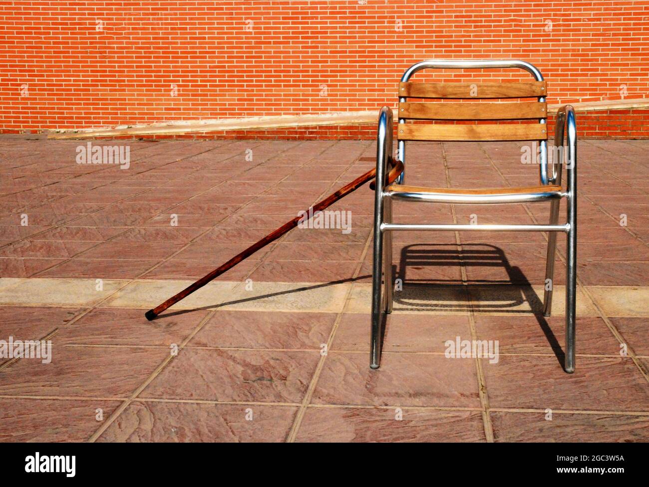 Chair on the street next to walking stick of elderly person, getting old Stock Photo
