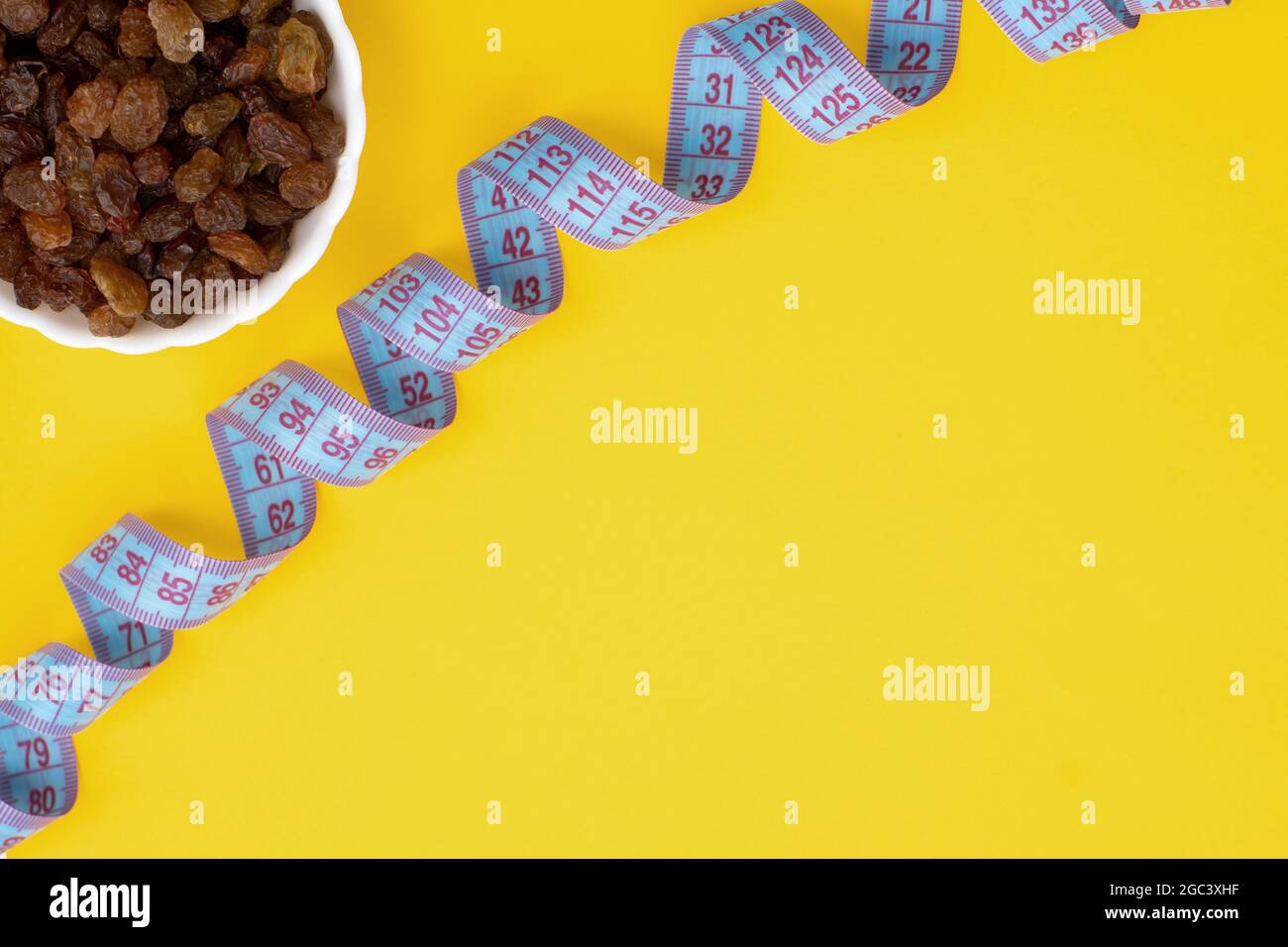 Close-up plate with dried fruits raisins and a centimeter tape. The concept of weight loss, healthy eating, overweight. Fitness menu. Top view. Flat l Stock Photo