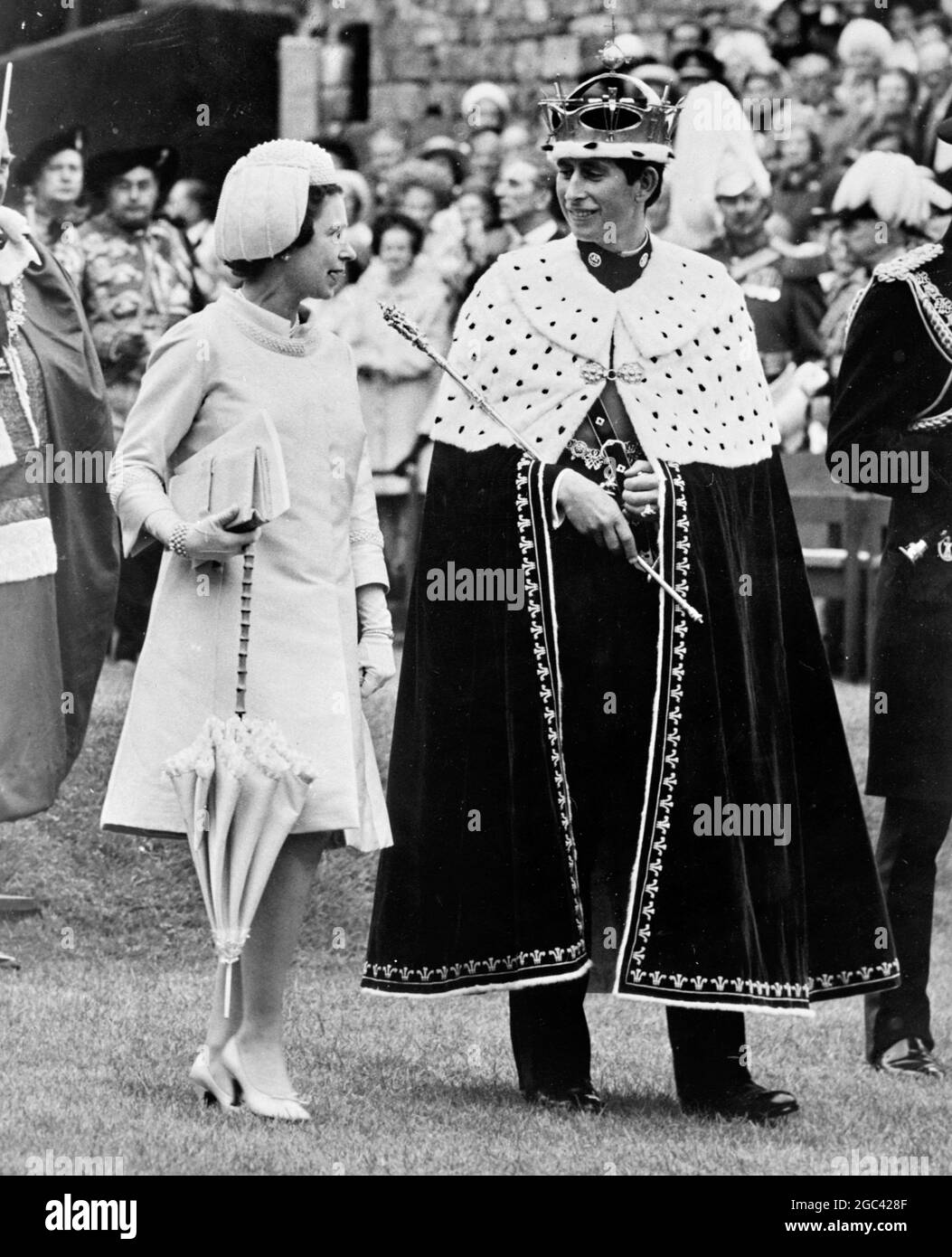 The pomp and ceremony over Queen Elizabeth II and her 20 year old son, the new Prince of Wales look at each other as they walk within the ancient ruins of the historic Caernarvon Castle at the end of the Investiture ceremony on 1 July 1969. Whilst the Queen carries just a parasol and Investiture documents, Prince Charles carries in his right hand the Gold Rod of Government, grips in his left hand the Sword symbolic of the Earldom of Chester and on his head, the jewelled, Gold Coronet - all are part of his insignia as the 21st Prince of Wales. 1 July 1969 Stock Photo