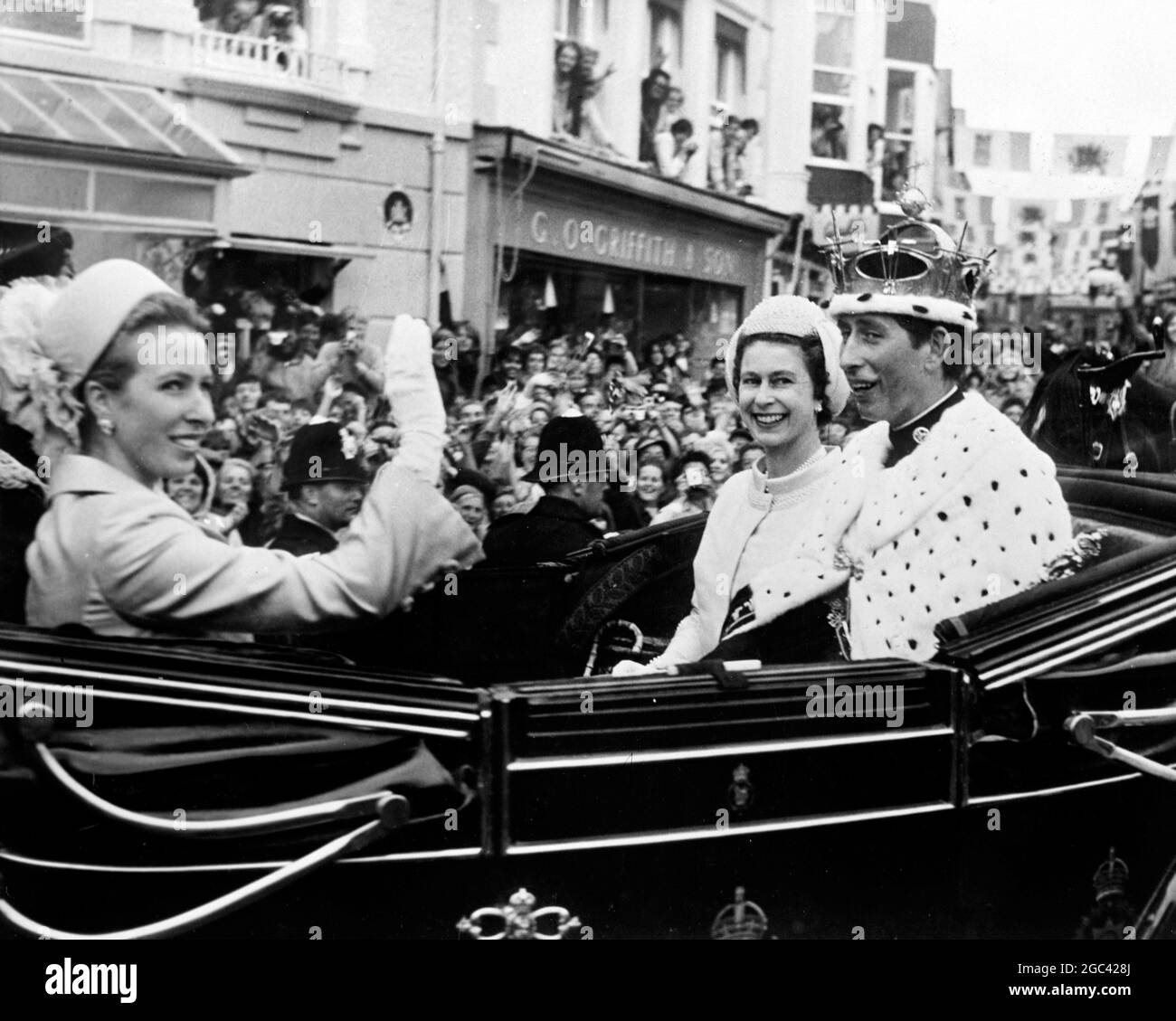 Princess Anne waves to the throng, as Her Majesty Elizabeth II steals a glance at her son, 20 year old Prince Charles, the newly invested Prince of Wales. The open state landau is seen leaving Caernarvon Castle following the colourful and historic ceremony yesterday 1 July 1969. It was the first time that the ceremony had taken place since 1911 when the present Duke of Windsor was invested as the Prince of Wales. 2 July 1969 Stock Photo