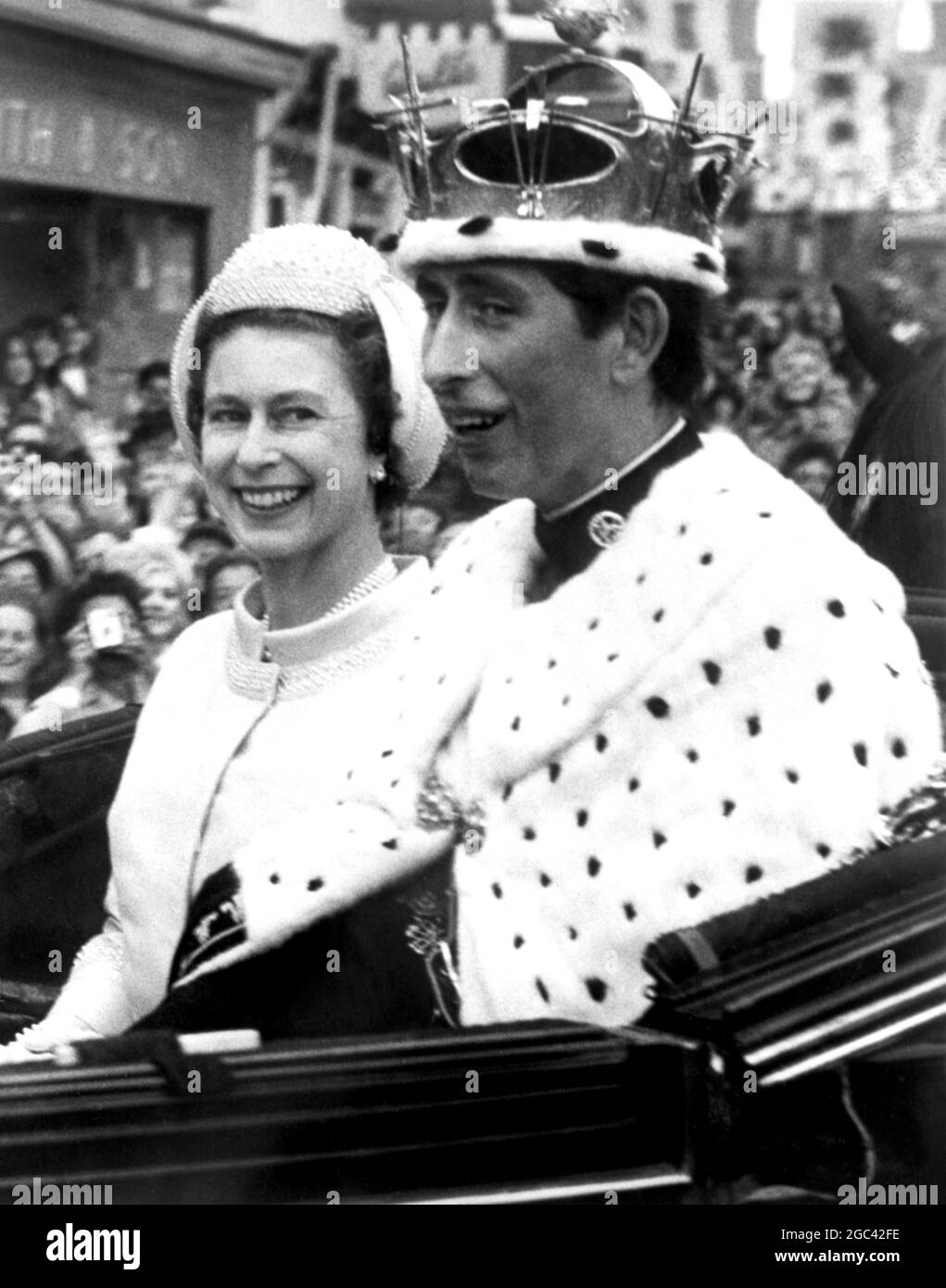 Queen Elizabeth II steals a quick glance at her happy, smiling son Prince Charles as their open state landau leaves Caernarvon Castle this afternoon following Charle's Investiture as the Prince of Wales. The historic ceremony was performed by the Queen on the Royal Dias inside the ancient walls of the Castle. The 20 year old, twenty first Prince of Wales is wearing a Gold Coronet, and a velvet and ermine mantle, part of the insignia. 1 July 1969 Stock Photo