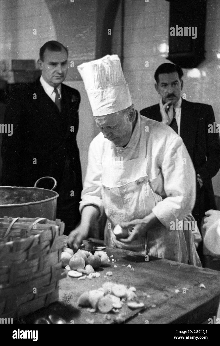 Behind the scenes at a state banquet. Homecoming banquet for Queen Elizabeth II at the Mansion House, London after her Commonwealth Tour in 1954. The catering firm of Ring & Brymer (Birch’s) Ltd have handled the catering at every Coronation banquet given by the Corporation of London since Queen Victoria’s Coronation and have catered for more crowned heads than any other firm in the world. 19 May 1954 Photo shows: Old Mr Hancock, preparing the stuffed apples to go with the Spring Chicken, is watched by Lindsay Ring (left, and Head Chef Mr Bigg. Stock Photo