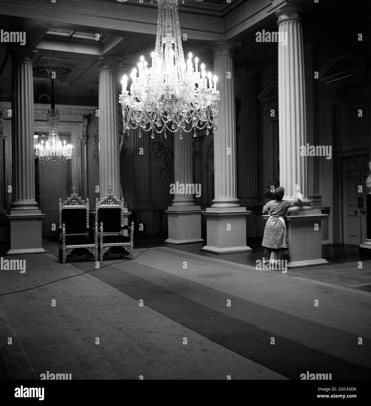 Behind the scenes at a state banquet. Homecoming banquet for Queen Elizabeth II at the Mansion House, London after her Commonwealth Tour in 1954. The catering firm of Ring & Brymer (Birch’s) Ltd have handled the catering at every Coronation banquet given by the Corporation of London since Queen Victoria’s Coronation and have catered for more crowned heads than any other firm in the world. 19 May 1954 Photo shows: Inside, in the Venetian Salon, a cleaner dusts the pillars. The chairs are those in which the Lord Major and the Mayoress – Sir Noel Bowater and Lady Bowater – will sit to receive the Stock Photo
