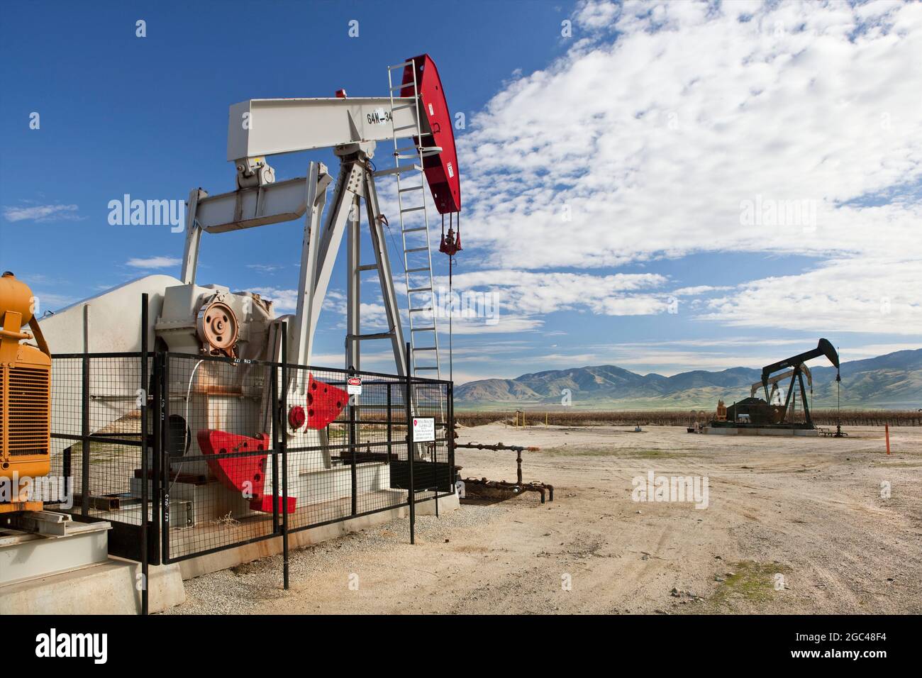 Oil wells with pumps and grape vines in distance at Kern Co. Stock Photo