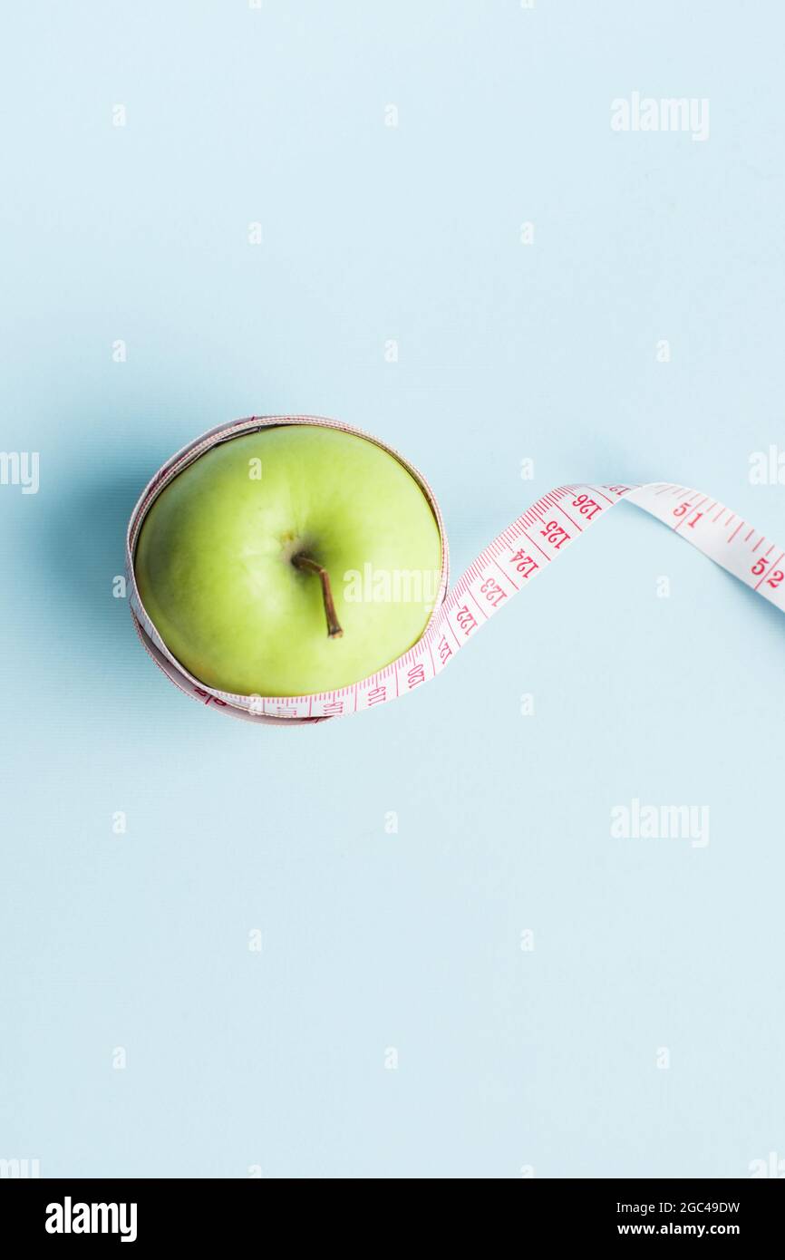 Apple with measuring tape on blue background. Weight loss, counting