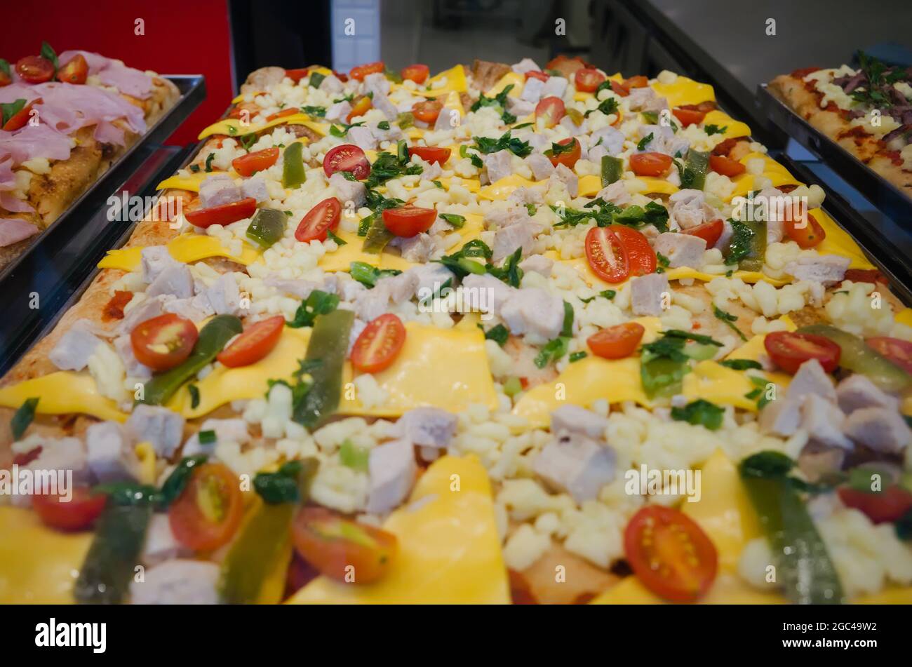 Square Sicilian pizza called Sfinchini on a tray in fast food restaurant. Square pizza with cherry tomatoes, cheese, cucumbers and chicken. Stock Photo