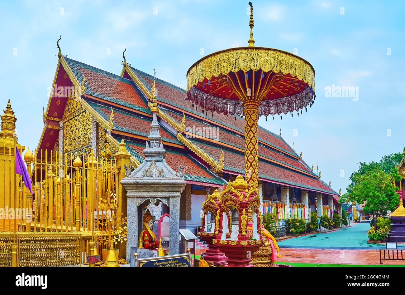 The stunning red-gilt chatra parasol with relief patterns, carvings and hanging Bo Tree sacred leaves in front of the Viharn Luang building of Wat Phr Stock Photo