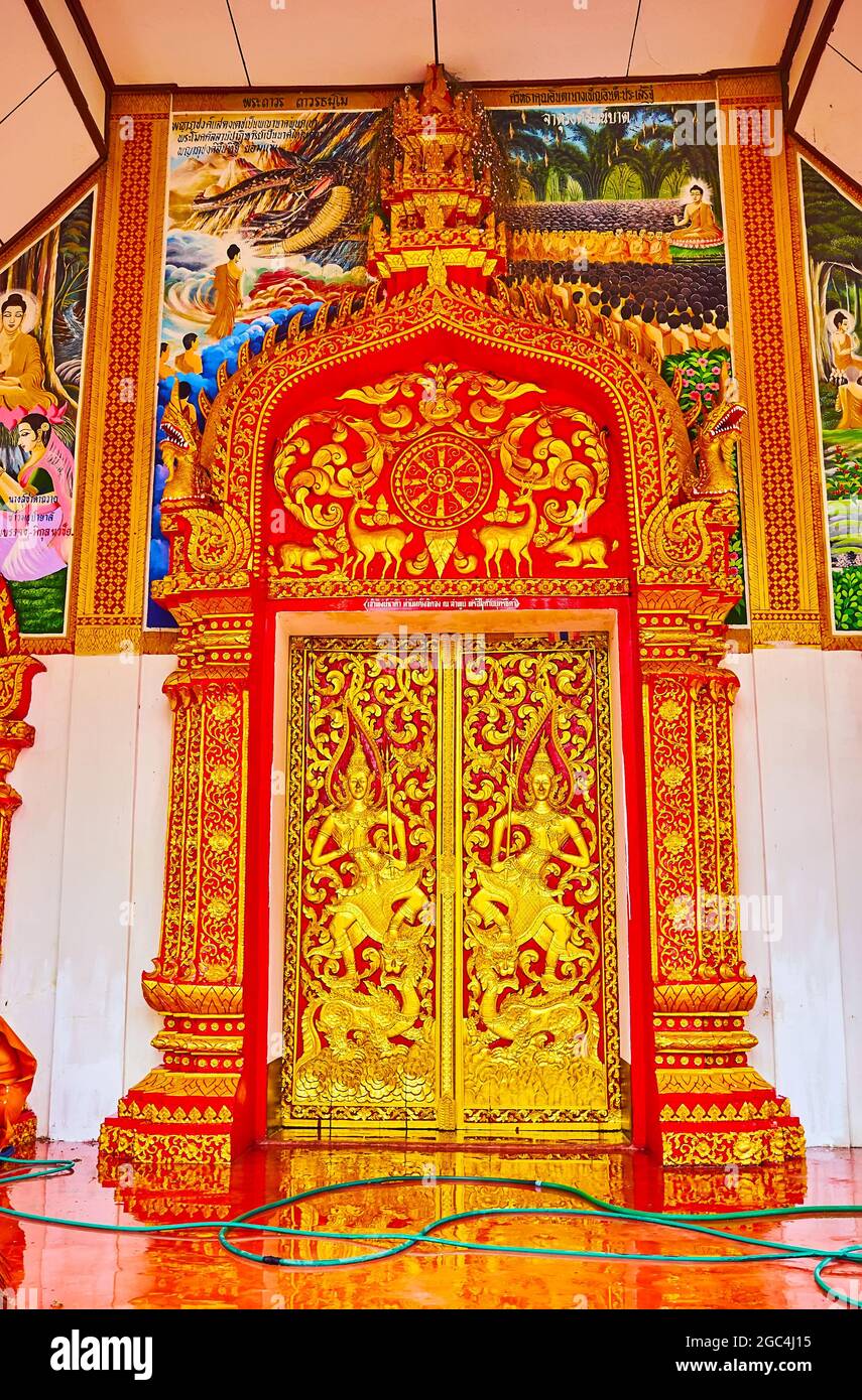 The outstanding entrance door of Wat Sangkharam Temple, decorated with intricate gilt patterns, wall sculptures of Kinnari, Wheel of Dharma and differ Stock Photo