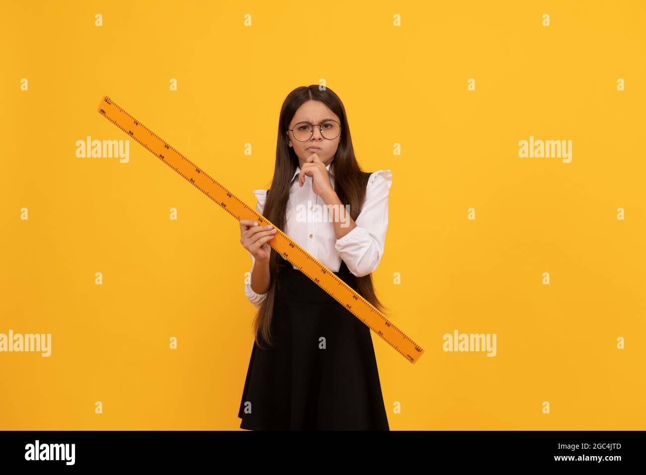 thinking teen girl in school uniform and glasses hold mathematics ruler for measuring, geometry Stock Photo