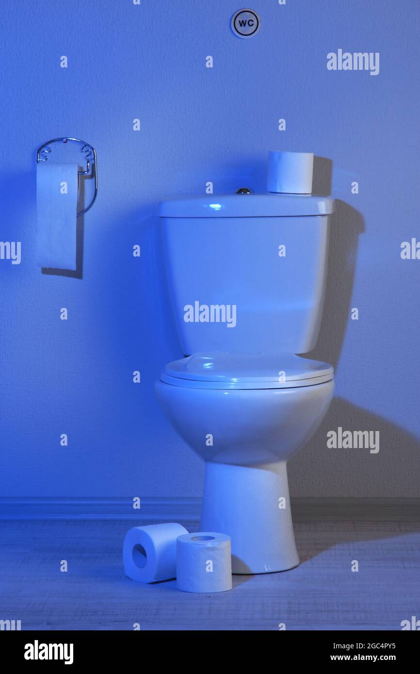 Toilet bowl and toilet paper in a bathroom with blue light Stock Photo