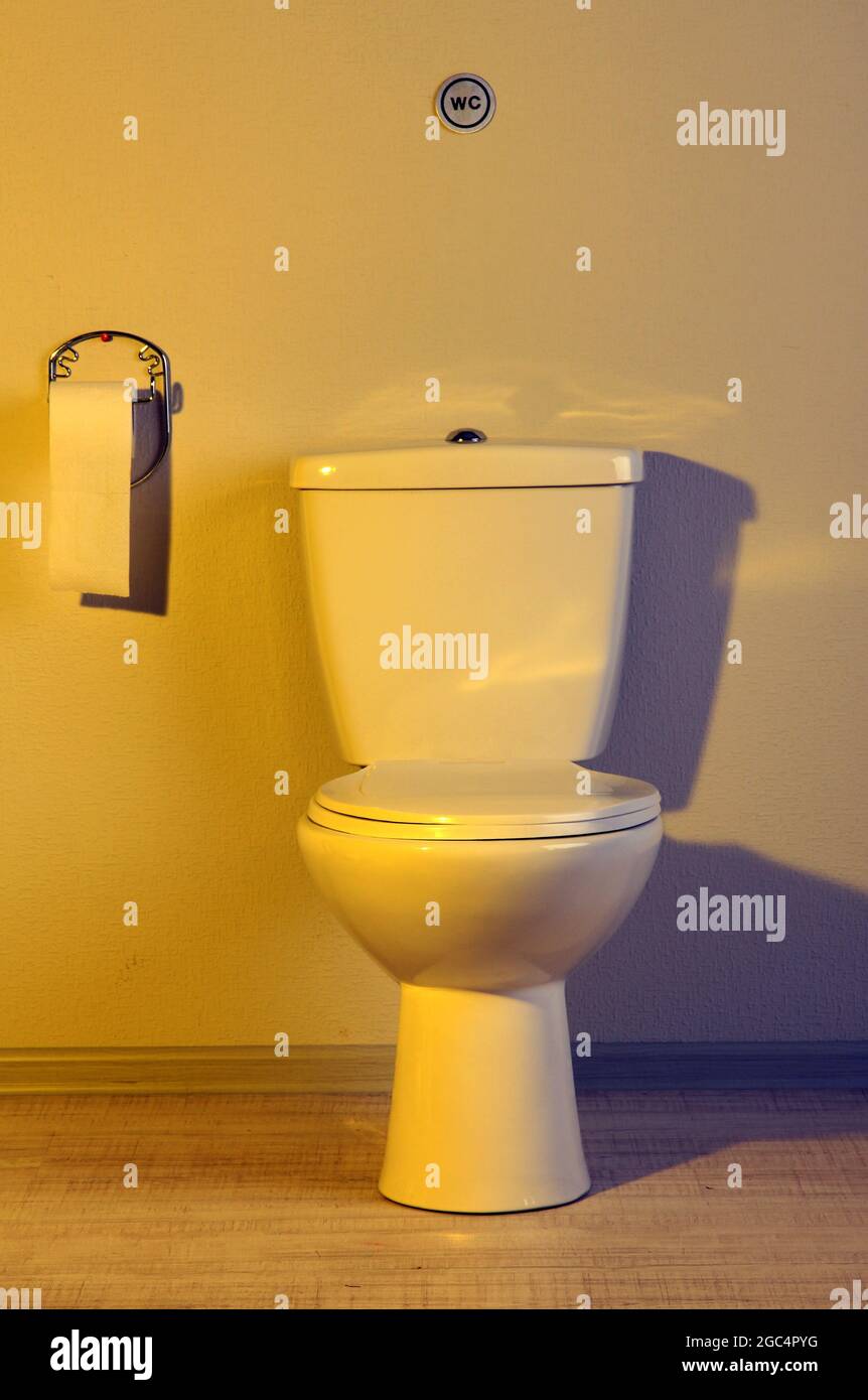 Toilet bowl and toilet paper in a bathroom with yellow light Stock