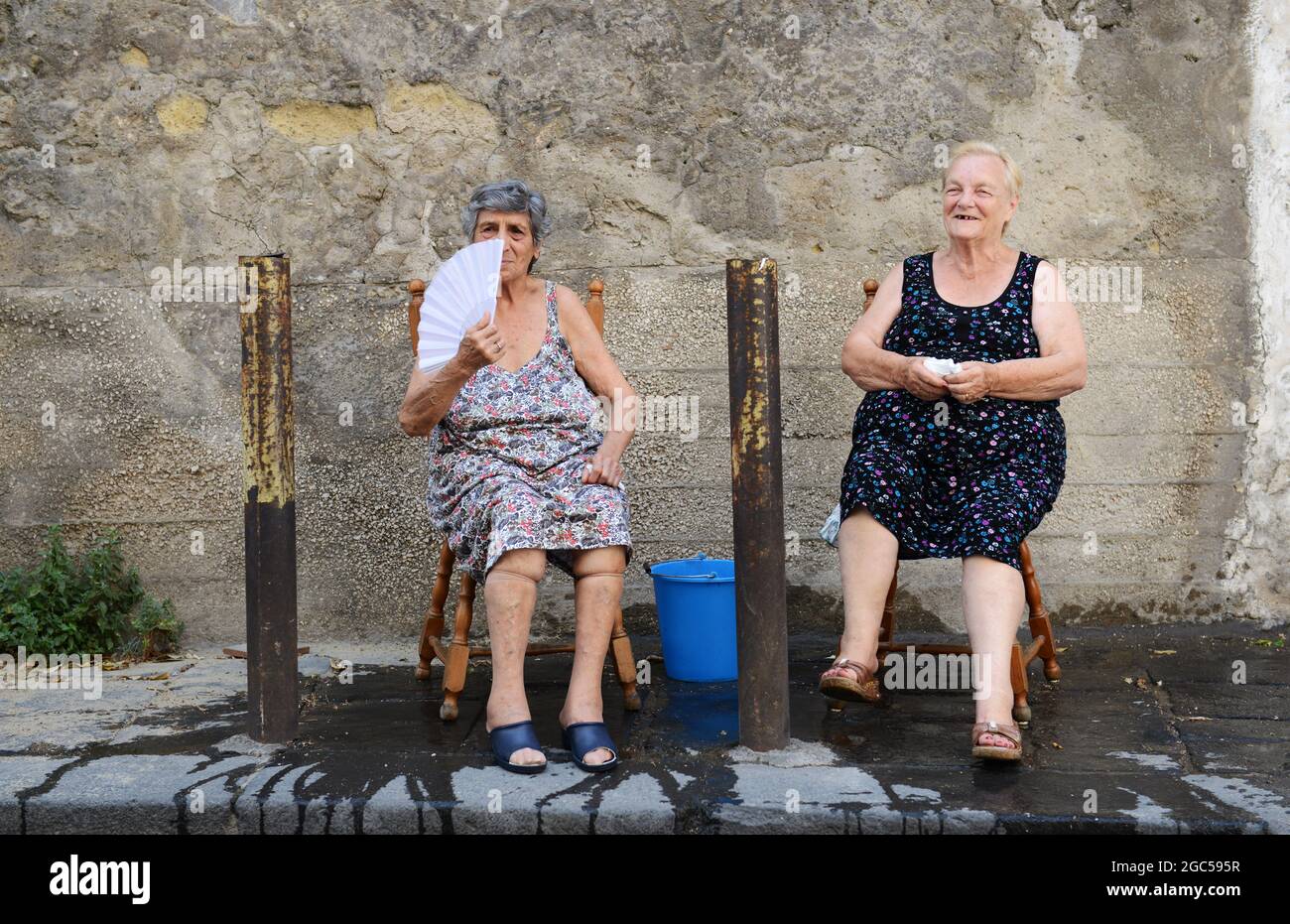 July 2015, Naples Italy. Elderly Italian women sitting outside on the street with a bucket of water to help with the scorching heat. Stock Photo