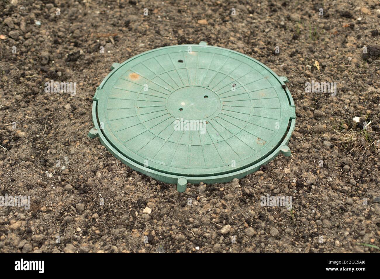 Sewer hatch in the ground. Round plastic cover to close access to sewer pipes. Green hatch of urban communications. Stock Photo