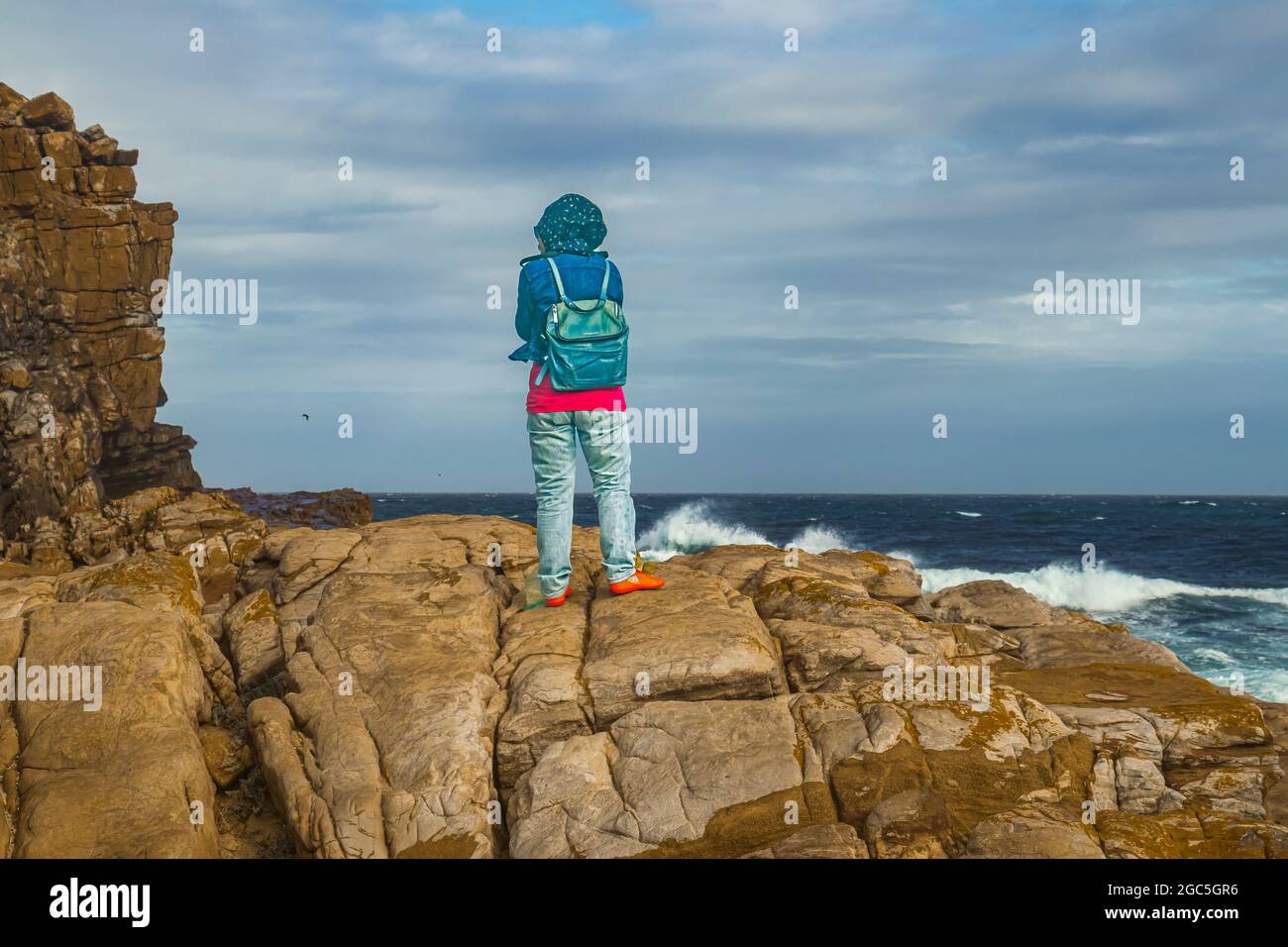 A woman standing on rock looking at wild sea of Atlantic Ocean at Cape of Good Hope in Cape Point National Park, South Africa. Stock Photo