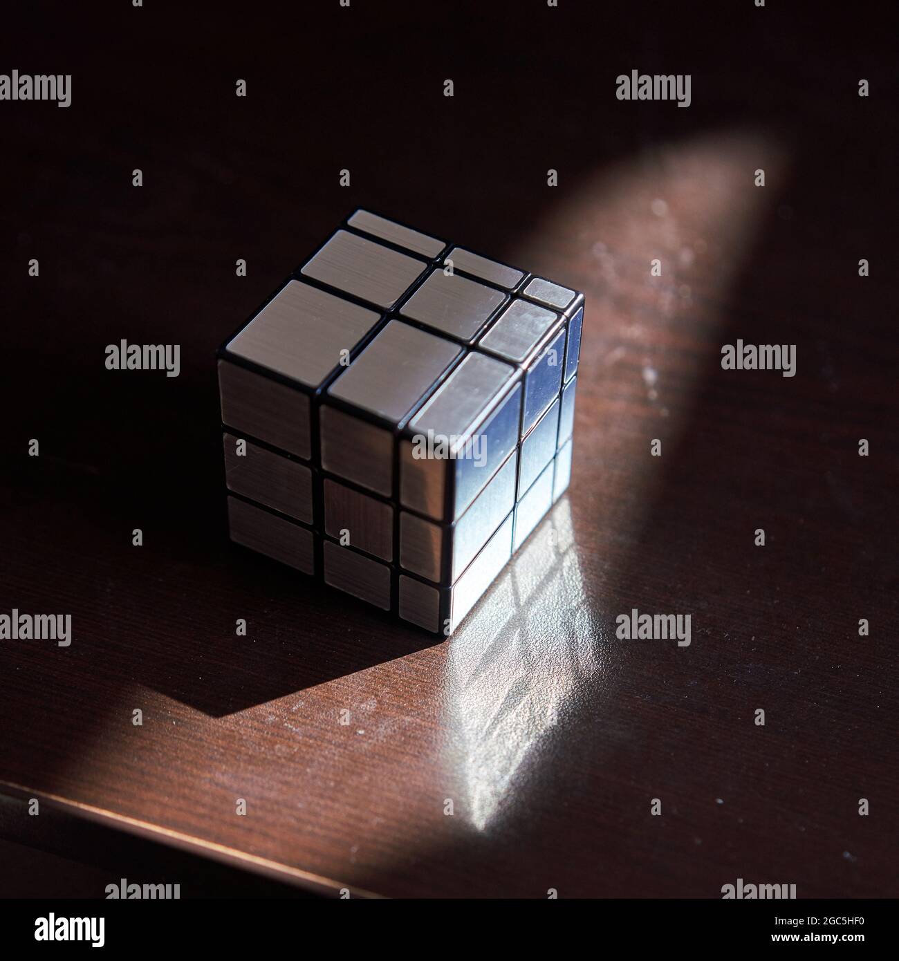 Mirror faces monotone Rubik's cube solved on tabletop with sunlight. Stock Photo