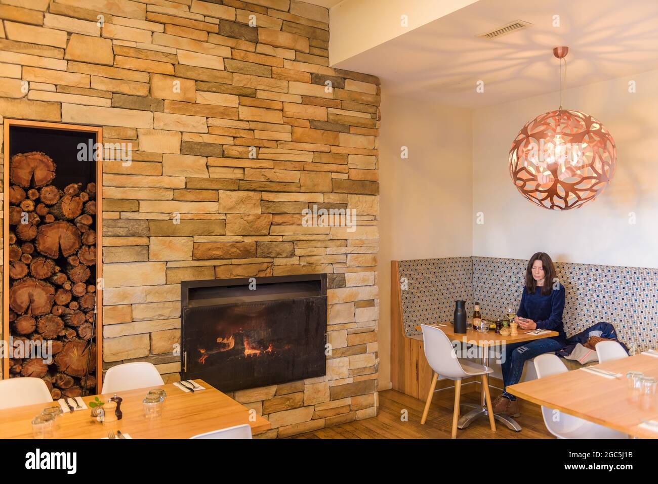 A female tourist sits in an alcove near a burning fireplace enjoying lunch at the 1802 restaurant at Coffin Bay, Eyre Peninsula in South Australia. Stock Photo