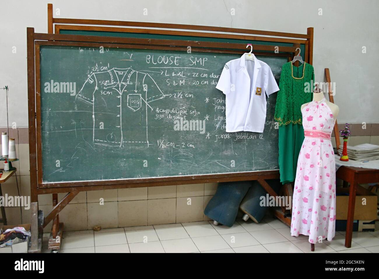 A green chalkboard with sewing instructions and some clothing samples in a classroom. Stock Photo