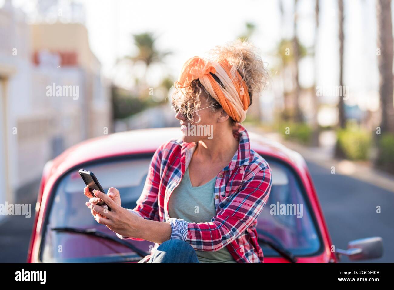 Woman using phone outdoor in real life - travel and summer holiday vacation with car for female driver - planning map destination or sending message a Stock Photo