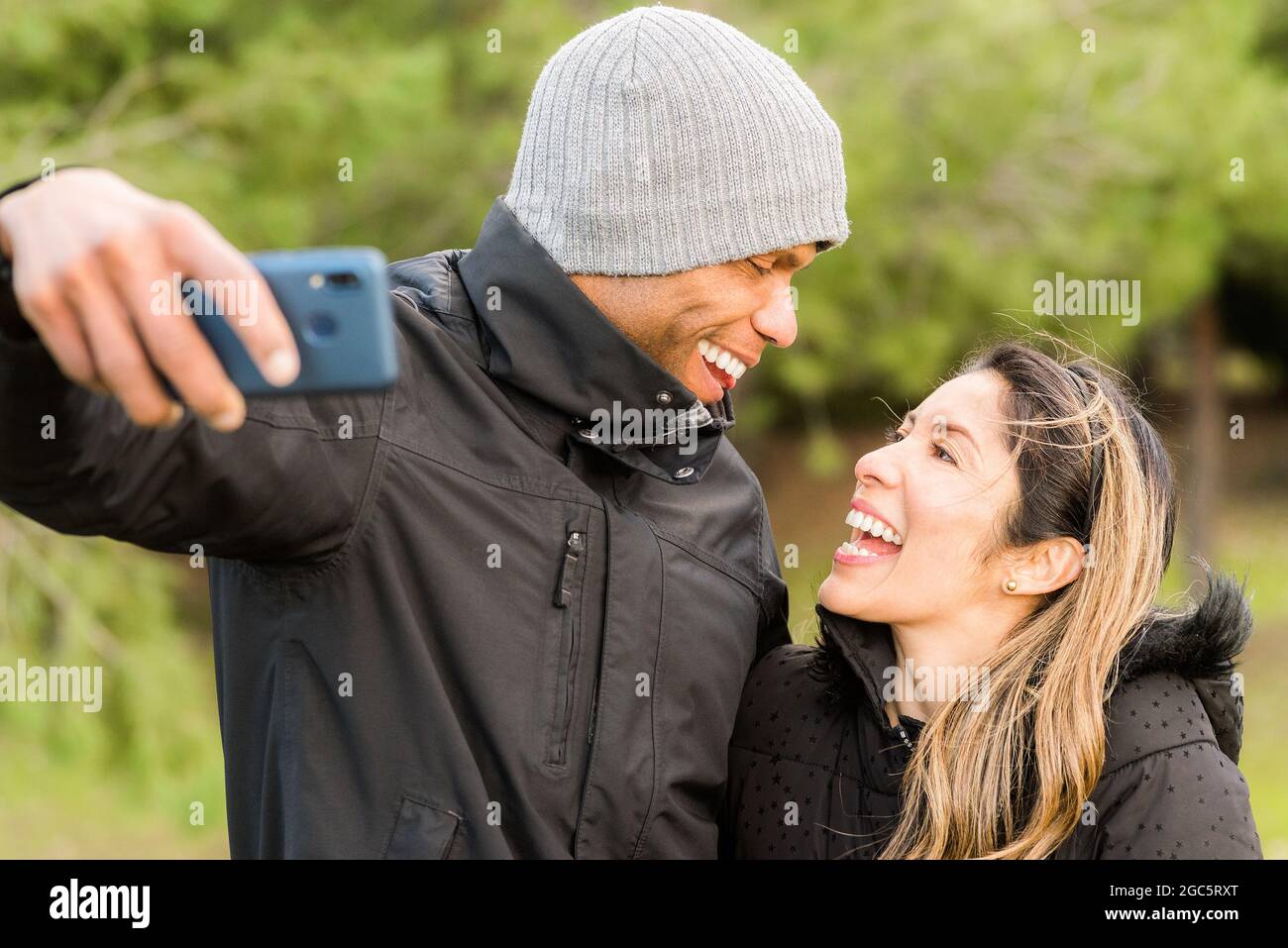 Fitness couple in warm clothes taking a selfie in the park looking at each other Stock Photo