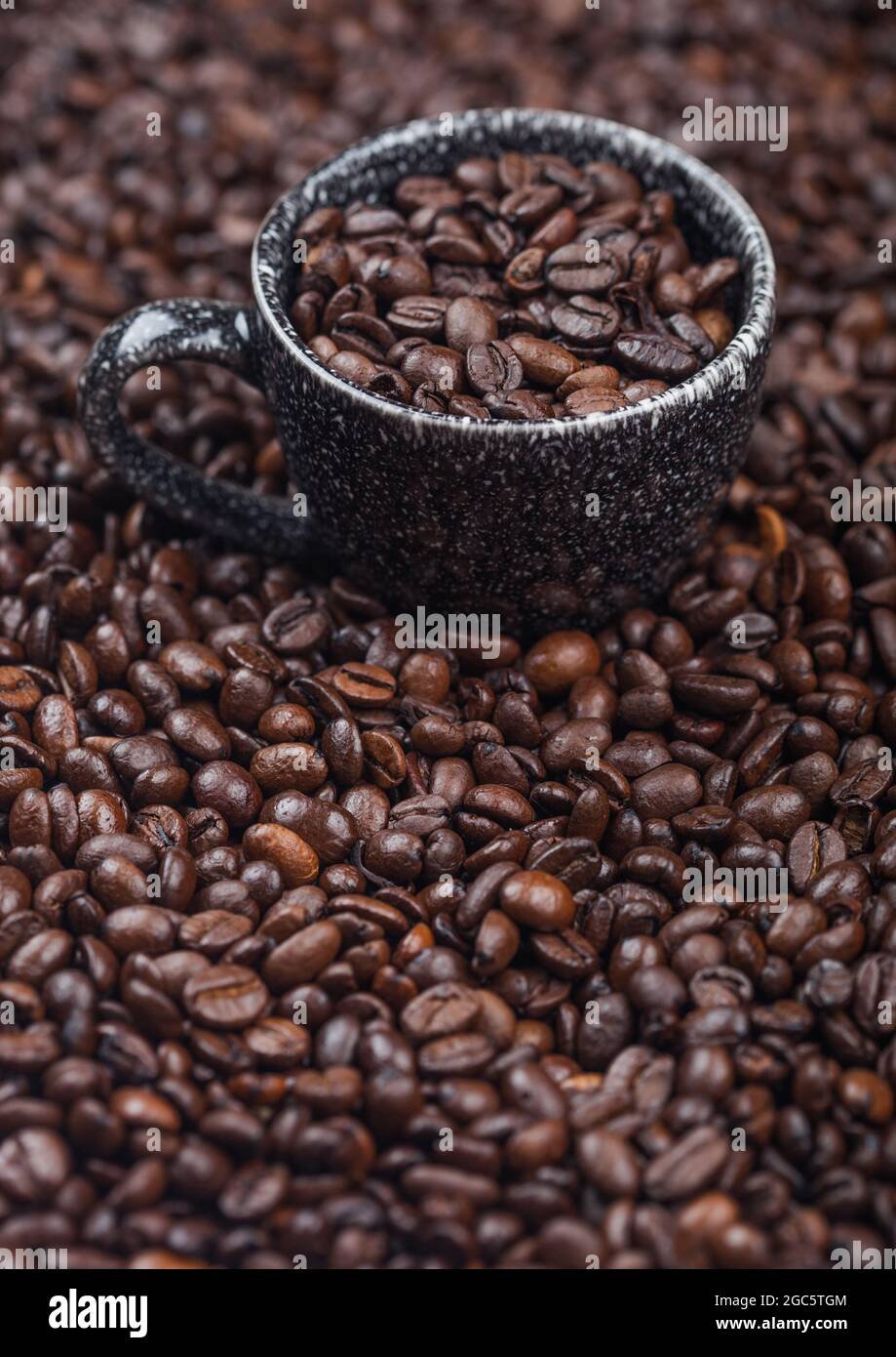 Black ceramic cup with fresh raw coffee beans inside beans background. Macro Stock Photo