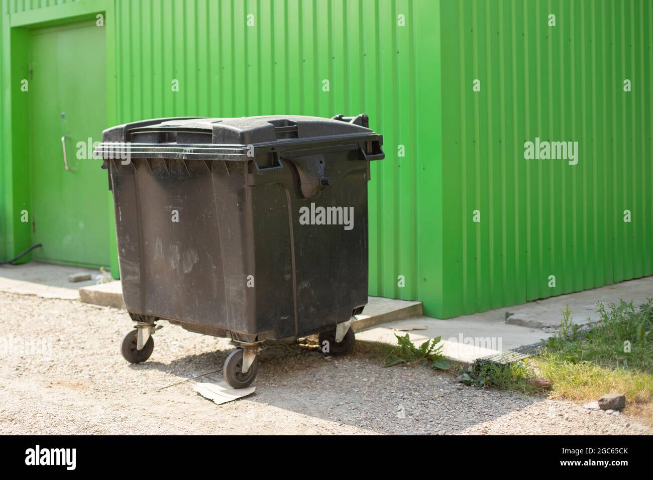 Garbage container on the street. One container for collecting waste. Black tank on wheels. Place of trash discharge. Stock Photo