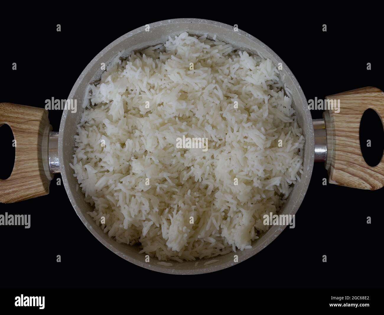 Bowl of cooked white long grain rice in a bowl with wooden handles and placed on a black counter top. Stock Photo
