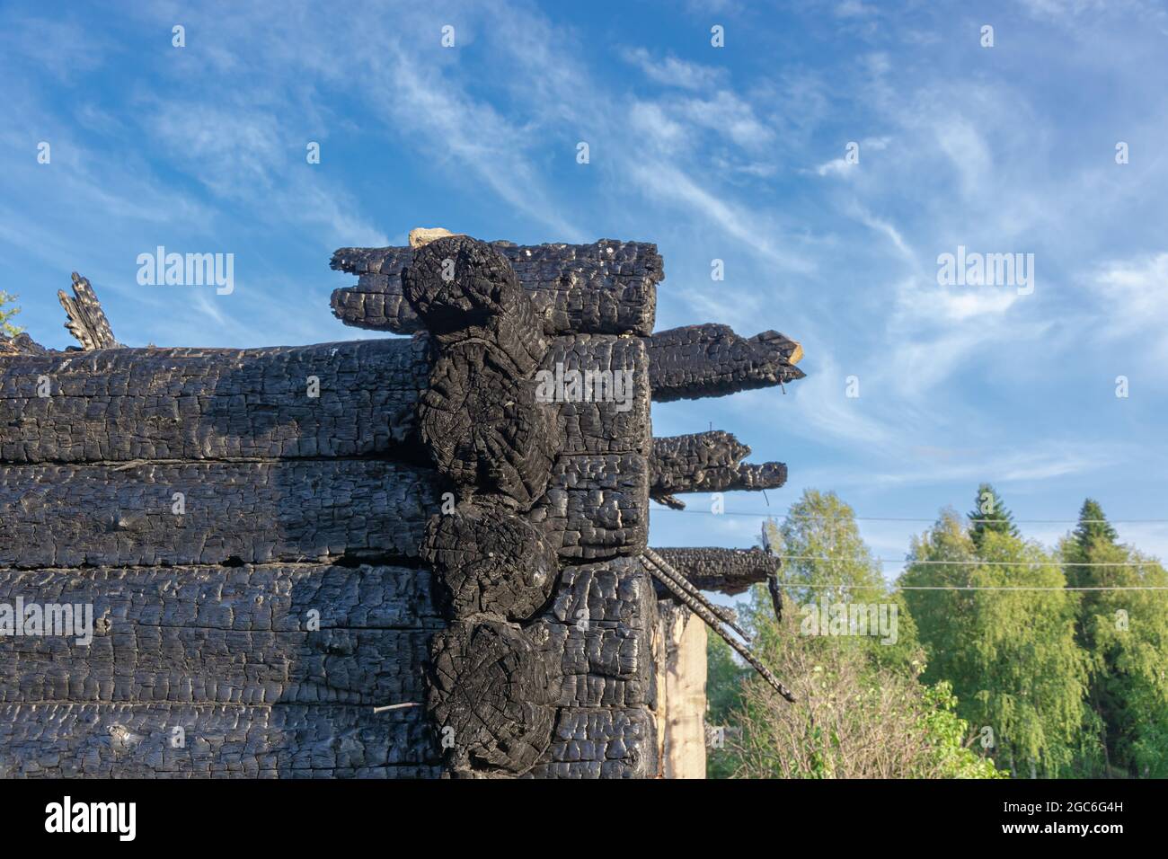 Burnt old log house in the village on a bright summer day against the blue sky. Close-up Stock Photo