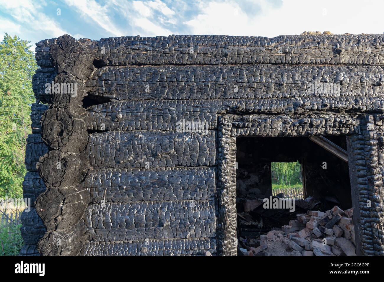 Burnt old log house in the village on a bright summer day against the blue sky. Close-up Stock Photo