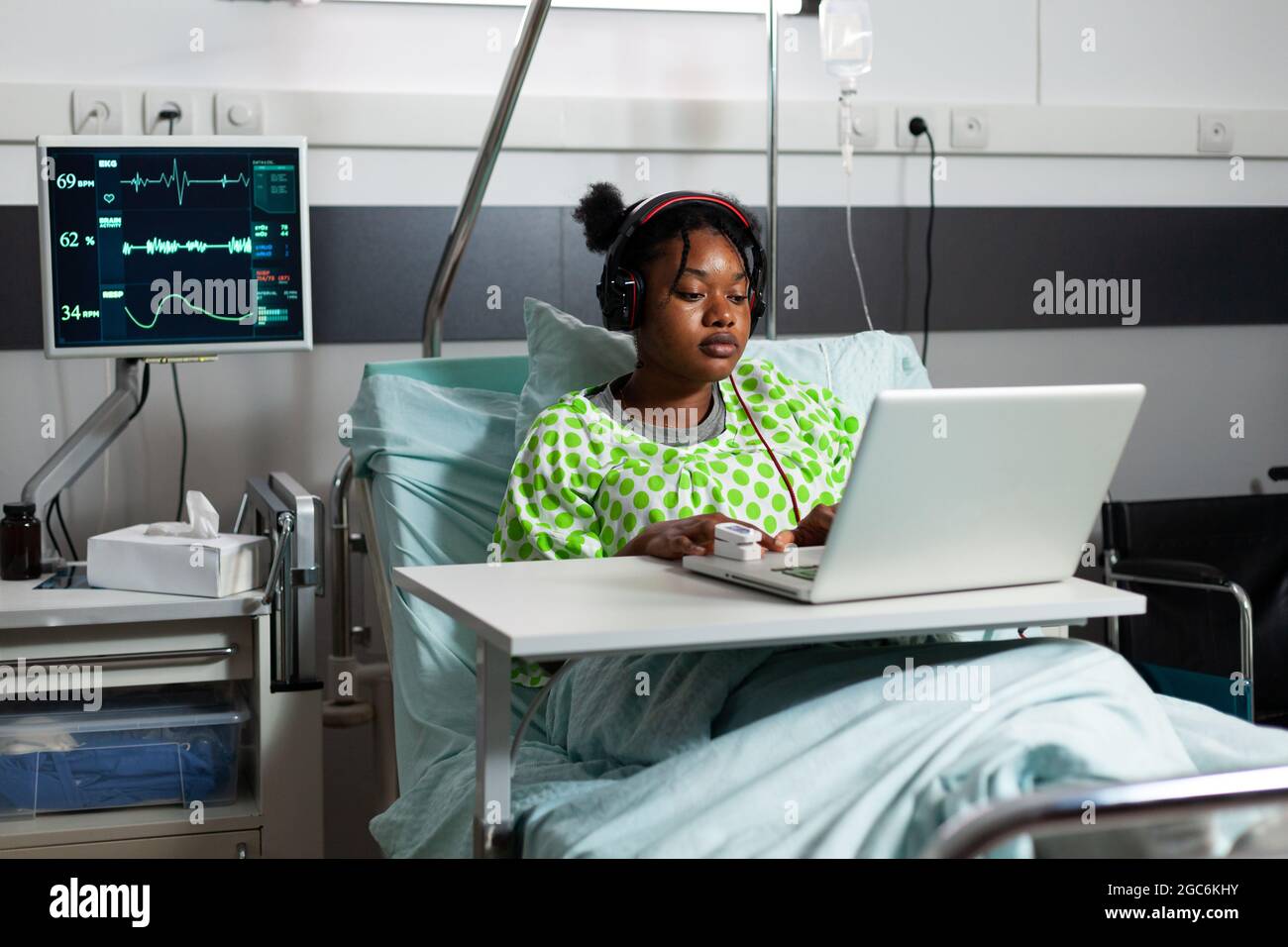 Sick young patient with headphones using laptop in hospital ward ...