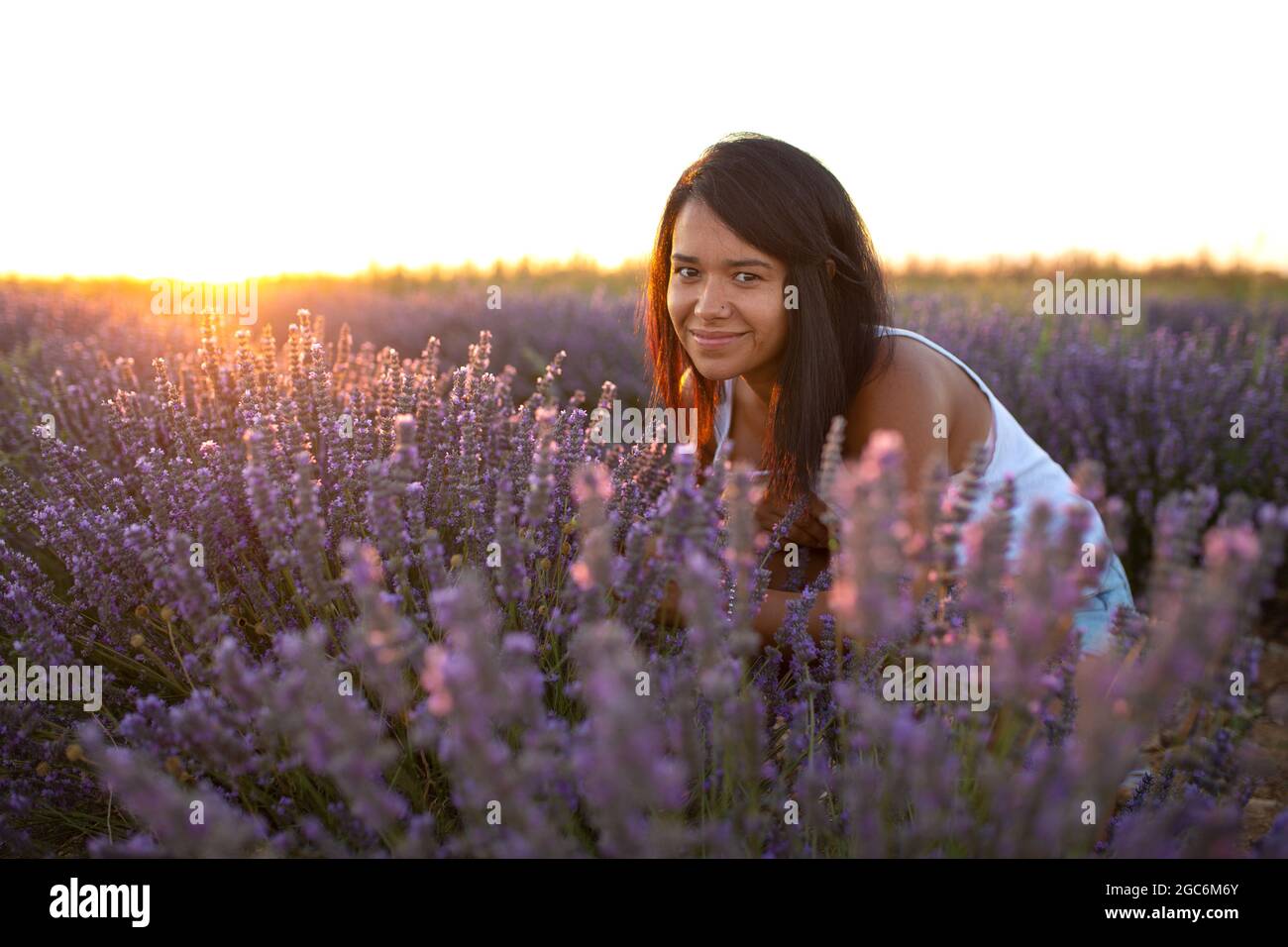 young latina woman looks at camera among lavender flowers at sunset Stock Photo