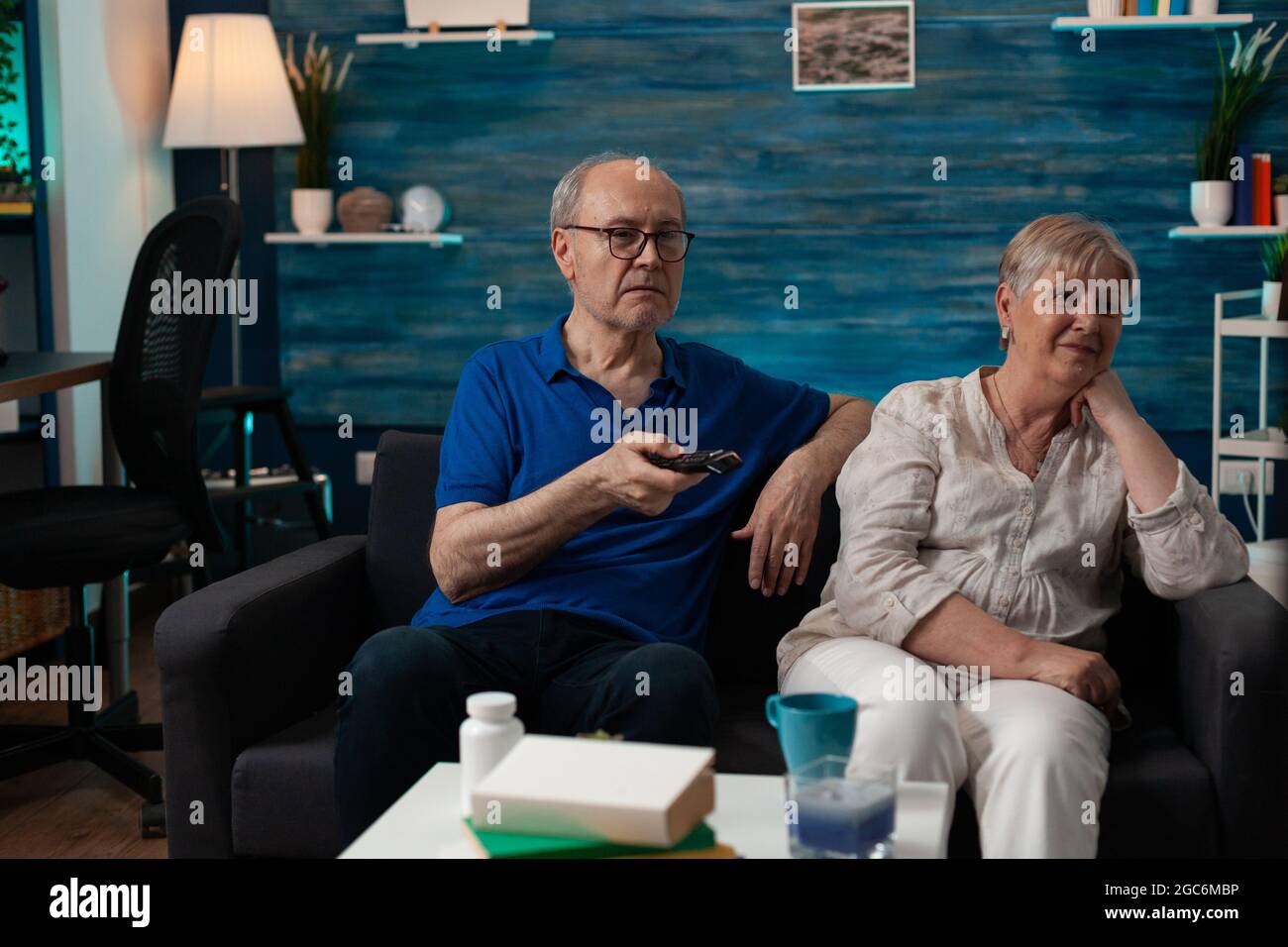 Old couple enjoying retirement at home sitting on sofa watching television. Senior people having fun together with tv movie technology for relaxation entertainment being indoors Stock Photo